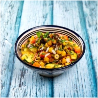 Vegan luchtige, gestoomde couscous met olijven, courgette, kikkererwten, pompoen, witte kool en wortel, aangevuld met gekarameliseerde ui, rozijnen, shakshouka en geurige bouillon. Deze heerlijke combinatie bevat seizoensgebonden groenten, zodat je altijd geniet van verse ingrediënten in al onze gerechten