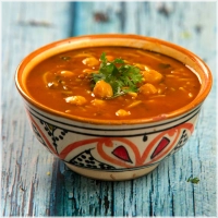 Harira, een voedzame en verwarmende Marokkaanse soep met tomaten, kikkererwten, linzen en kruiden. Verkrijgbaar als vegetarische optie of met vlees of kip. Gekenmerkt door zijn rijke smaak en vullende eigenschappen, geserveerd met brood en ideaal met dadels<br>